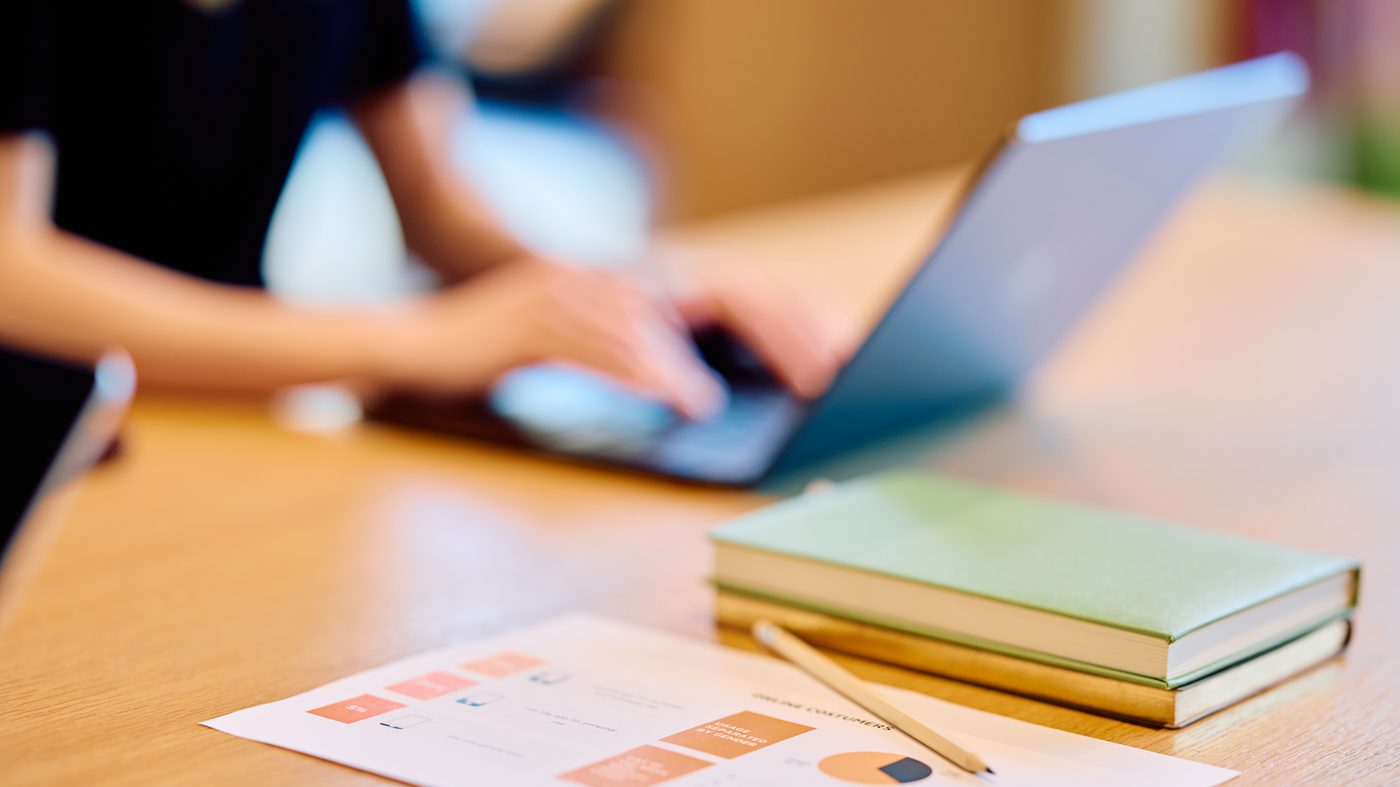 Hands working at a laptop beside printed documents